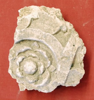 A fragment of decorative plasterwork with a Tudor rose within stripwork. The fragment is about 8cm across
